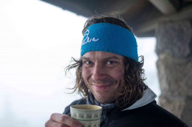 Sebastian Förth trägt ein Stirnband und lächelt in die Kamera während er einen Tee trinkt