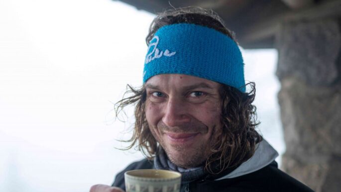 Sebastian Förth trägt ein Stirnband und lächelt in die Kamera während er einen Tee trinkt