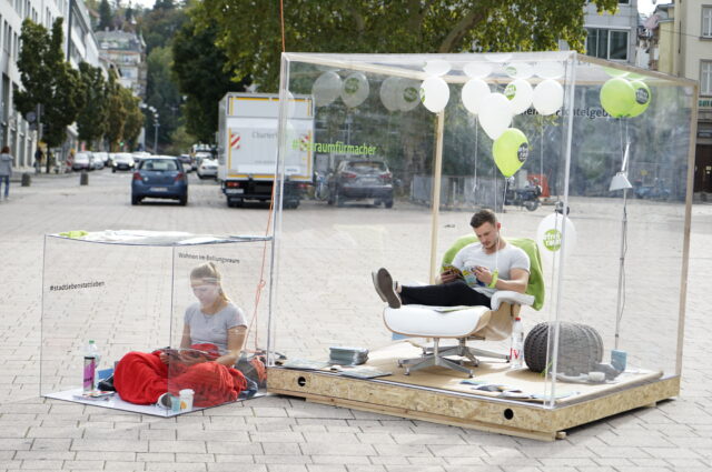 Zwei Personen sitzen im Glaskasten in der Stuttgarter Innenstadt