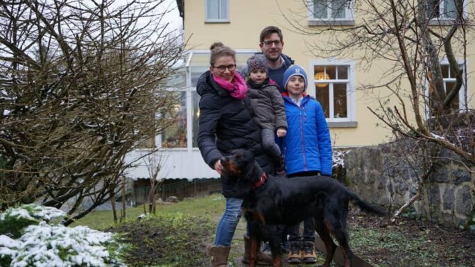 Melanie Schiener mit Mann und zwei Kindern und Hund stehen im Garten im Winter alle sind winterlich angezogen und die Sträucher sind mit Schnee bedeckt