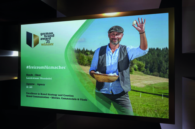Sieger des German Brand Award mit einem Bild von Werner wie er ein Ei in die Luft hält und fröhlich in die Kamera lächelt