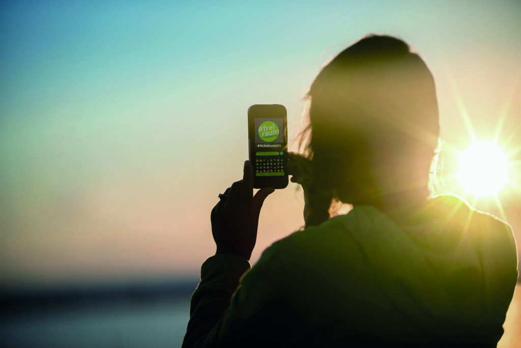 Frau im Sonnenuntergang mit Smartphone und Freiraum App